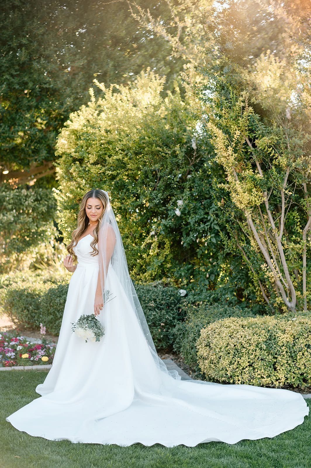 Bride in white wedding dress and veil holding bouquet in lush garden setting