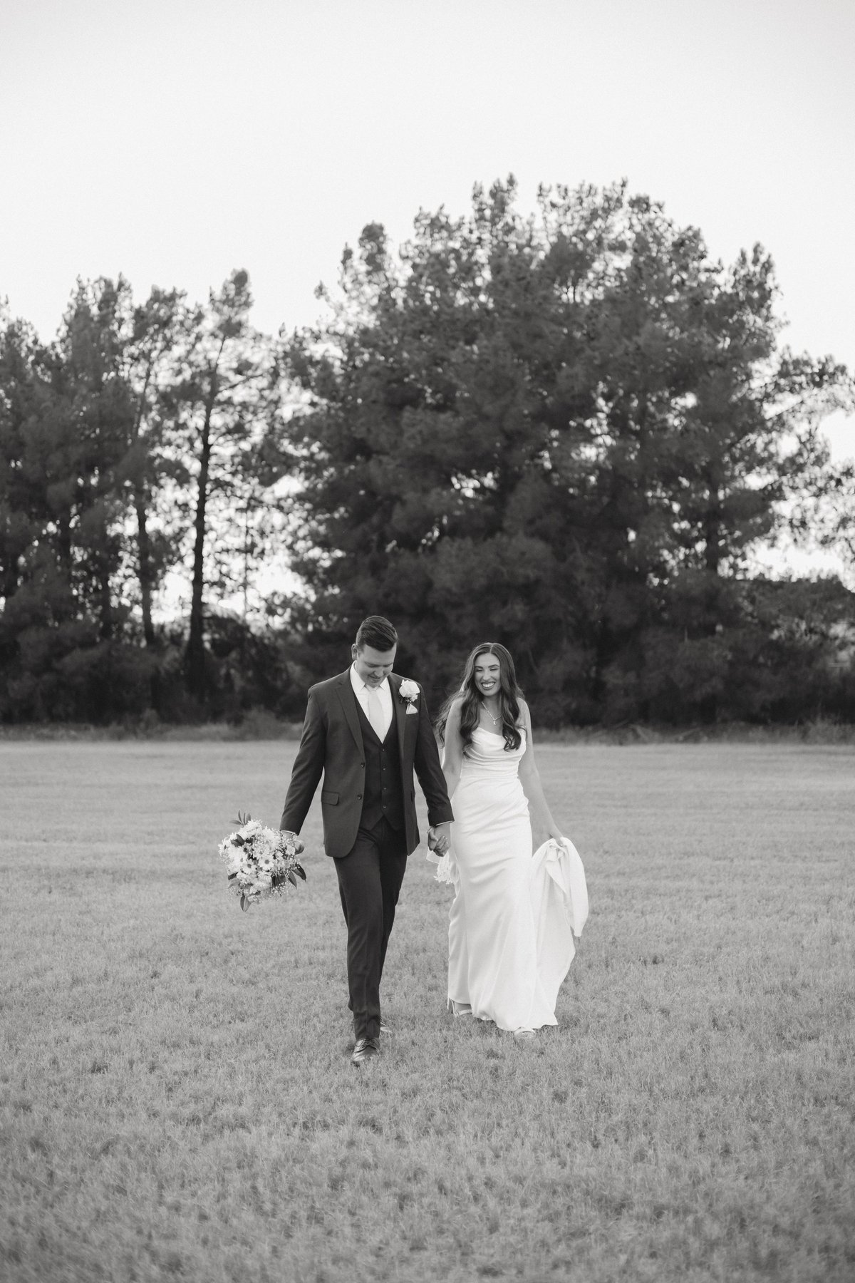Bride and groom holding hands walking through an open field in black and white wedding photograph