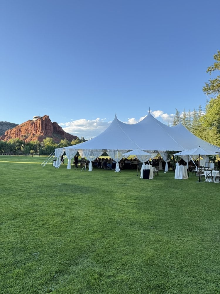White tent event setup on green lawn with red rock formations and mountains visible in the background under blue sky